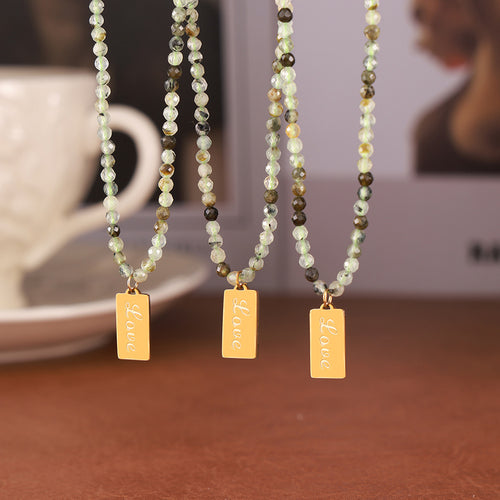 Three green stone bead necklaces with gold Love tags hanging in row