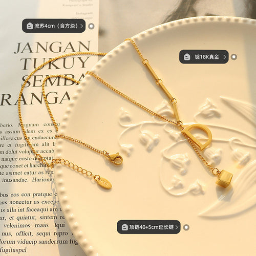 Gold D letter necklace flat on plate with tassel length plating tags