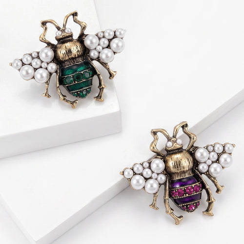 Green and purple pearl-wing bee brooches on white stepped blocks