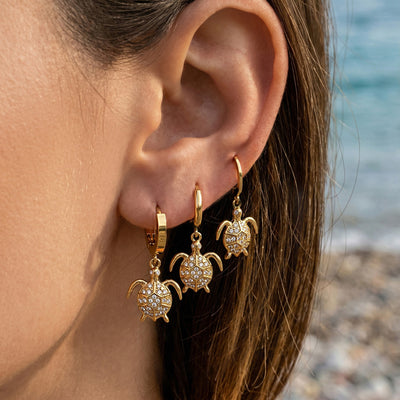 Three gold crystal turtle dangle hoops worn stacked on one ear by beach