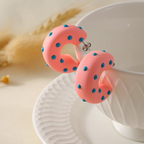 Pink blue-dot C hoop earrings propped on white cup and plate