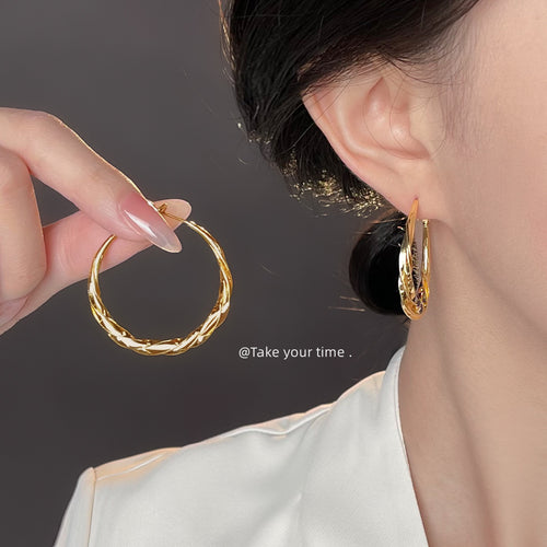 Gold twisted rope hoop held beside matching hoop worn on ear
