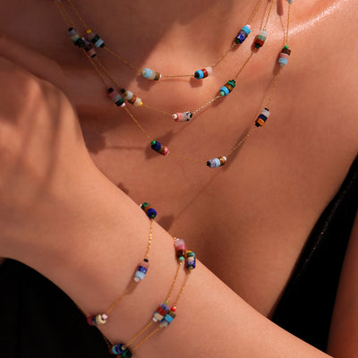 Layered gold natural stone bead necklaces and bracelets worn at beach
