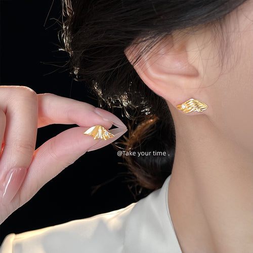 Gold feather wing stud worn on ear, matching stud held in hand