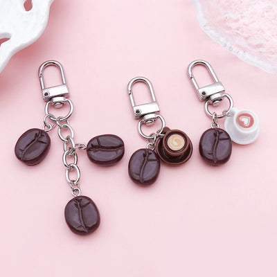 Three coffee-themed keychains arranged on a pink background.
