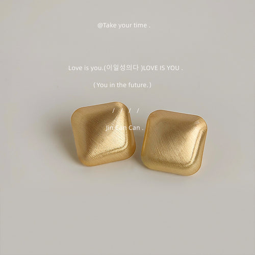 Gold brushed matte square diamond studs on gray surface