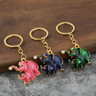 Three rose red, blue, and green paired elephant keychains displayed on a wood and gray surface.