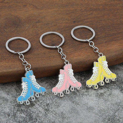 Sky blue, pink, and yellow roller skate keychains arranged on wood and gray fabric.