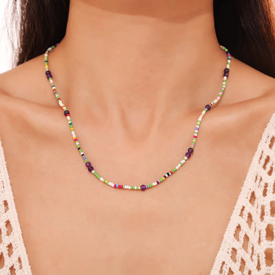 Model wearing multicolor seed bead necklace with purple stone accents at neckline