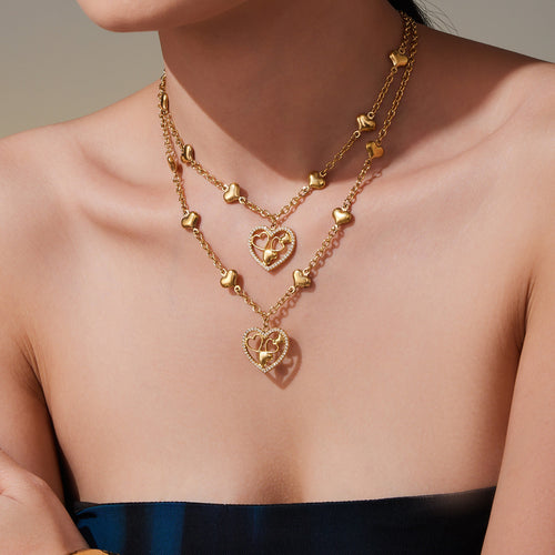 Model wearing layered gold heart station necklaces on bare collarbone