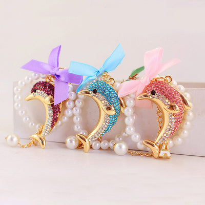 Three rhinestone dolphin keychains in purple, blue, and pink with matching ribbon bows and pearl-look strands.