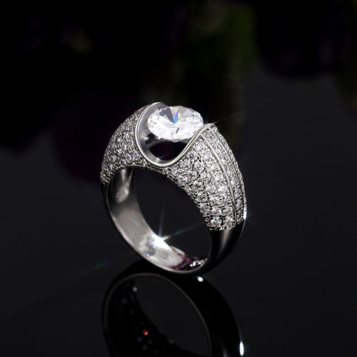 wide pavé ring with raised round center stone shown from a side angle