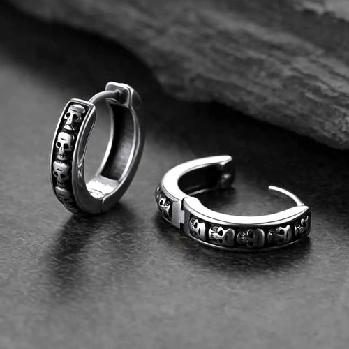 Open and closed silver skull huggie hoops on slate surface