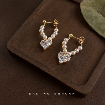 Gold pearl U loop heart zircon earrings on dark wood tray