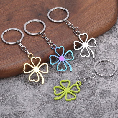 Gold, silver, light green, and iridescent clover keychains are arranged on wood and gray fabric.
