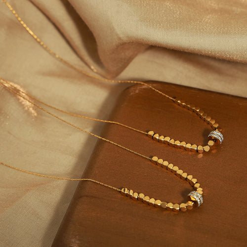 Two gold hexagon bead necklaces draped on brown tray fabric