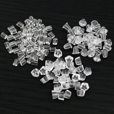 Front overview of clear plastic stud earring backs in assorted shapes arranged on a light background