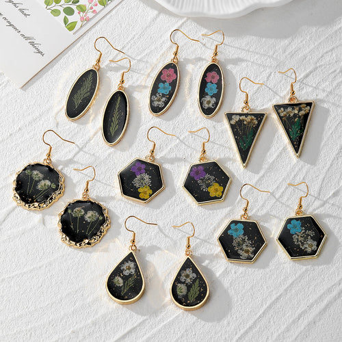 Seven pairs of black geometric resin dried flower earrings on white surface