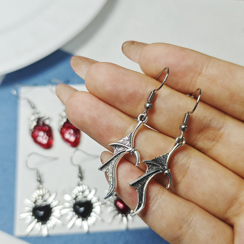 Hand holding silver bat wing drop earrings with heart pairs in background