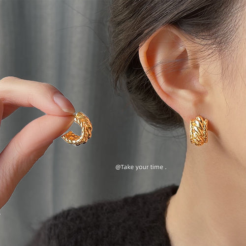 Model wearing gold braided C hoop stud while holding matching earring