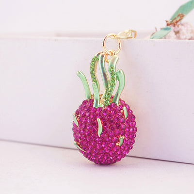 Front view of a pink rhinestone dragon fruit charm with green leaves and gold-tone details.
