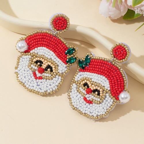 Pair of beaded Santa Claus face drop earrings with pearl accent on cream background