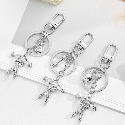 Three antique silver weightlifter keychain designs displayed together with money bag, dumbbell, and round weight charms
