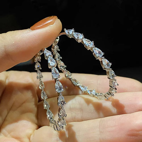 Pair of pear stone large hoops held open in palm against dark