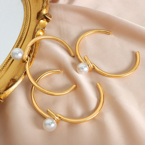 Three gold pearl twist open cuff bracelets on pink fabric near mirror