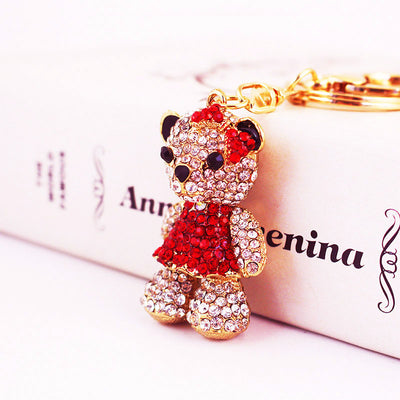 Side view of a red-dressed rhinestone bear charm resting against a printed box.