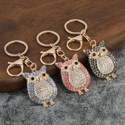 Black, pink, and blue rhinestone owl keychains arranged on a wooden surface.