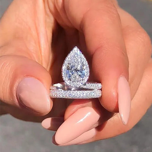 White gold pear halo wrap ring held between fingers outdoors
