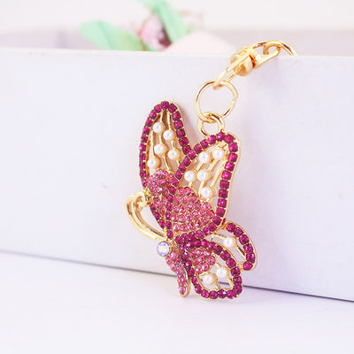 Pink rhinestone butterfly charm with white pearl-look beads on a gold-tone clip.