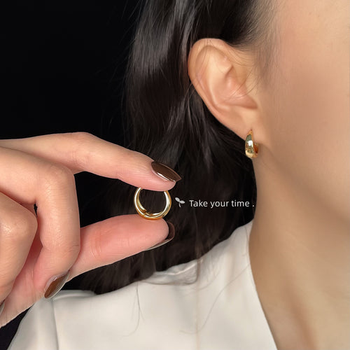 Model wearing gold huggie hoop, second hoop held in fingers