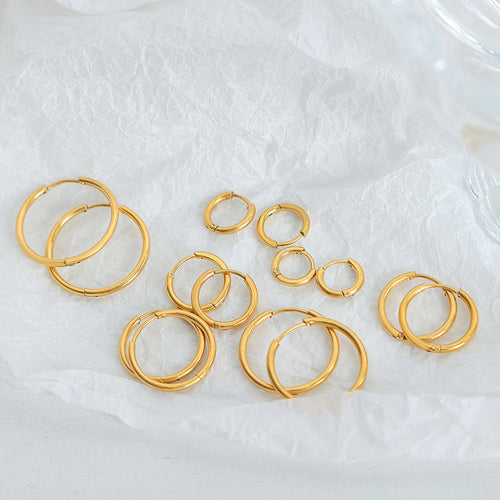 Assorted gold plain round hoop earrings scattered on white tissue