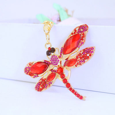 Red and pink jeweled dragonfly shown at an angle on a white background.