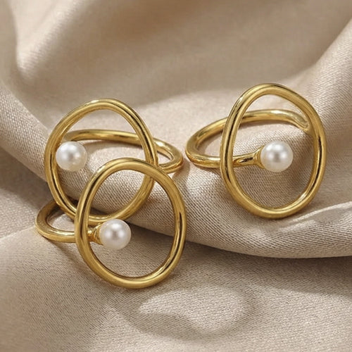 Three gold open oval pearl rings clustered on champagne fabric