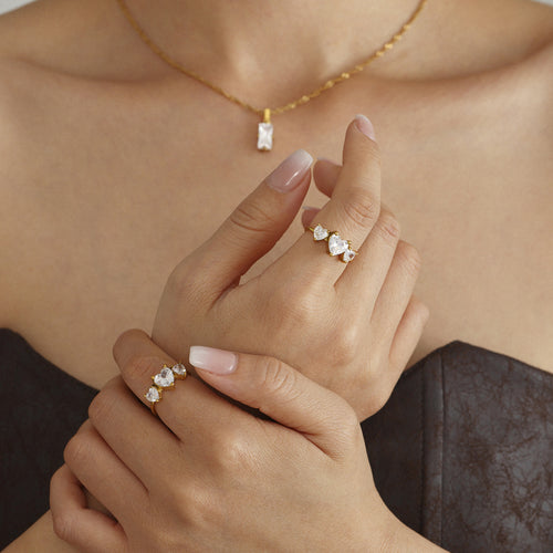 Hands wearing gold three heart zircon rings with necklace