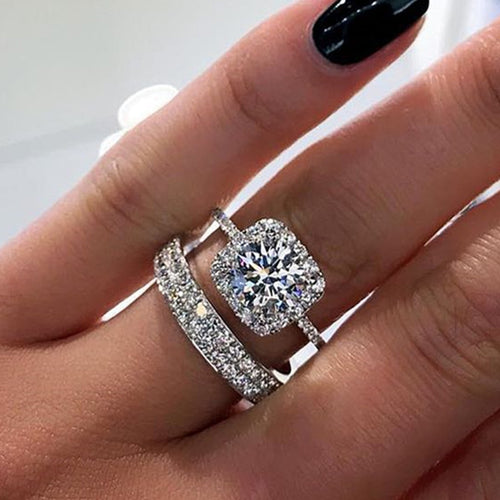 Silver-tone round solitaire halo two-ring set worn on a hand