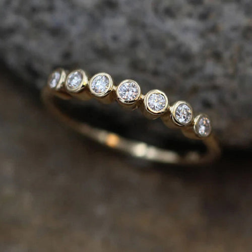 Angled view of gold bezel-set seven stone thin band ring