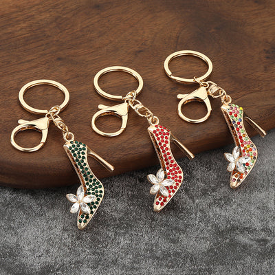 Three gold-tone high heel shoe keychains with green, red, and multicolor stones on wood.
