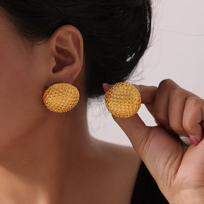 Model holding gold pyramid-texture dome stud earring next to ear