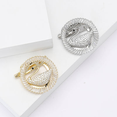 Gold and silver circular swan brooches on white blocks