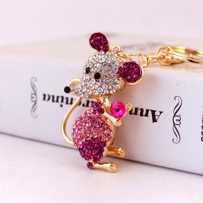 A pink rhinestone mouse holds a bright pink faceted stone beside gold-tone key hardware.