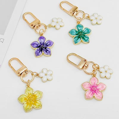 Four enamel flower keychains in purple, teal, yellow, and pink, each with a small white flower charm