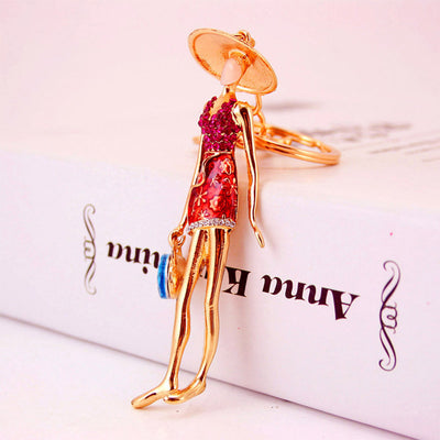 Side view of a gold-tone woman figure wearing a red dress and holding a blue handbag charm.