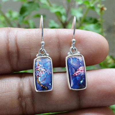 Silver blue abstract rectangle drop earrings held in hand outdoors