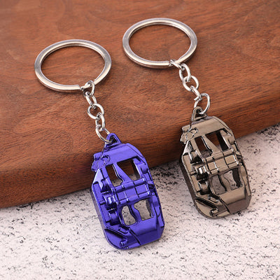 Blue and gunmetal brake caliper keychains rest side by side on a wood surface.