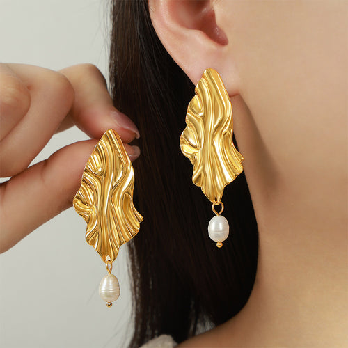 Model holding gold wavy leaf pearl drop earring near ear