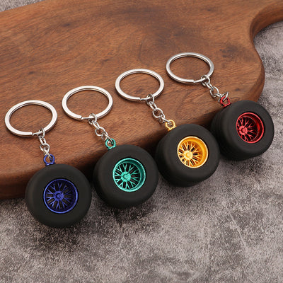 Four black tire keychains display deep blue, green, gold-tone, and red spoke centers on a wooden board.